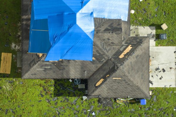 Top view of leaking house roof covered with protective tarp sheets against rain water leaks until replacement of asphalt shingles. Damage of building rooftop as aftermath of hurricane Ian in Florida.